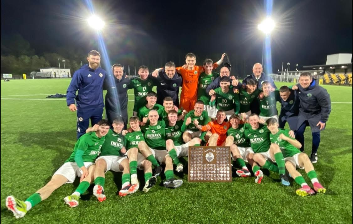 The Northern Ireland schools' squad and staff celebrate with the shield under floodlights